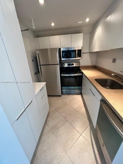 kitchen with stainless steel appliances, light tile flooring, white cabinetry, and sink