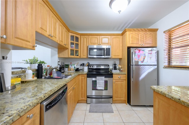 kitchen with light tile floors, light stone countertops, sink, and stainless steel appliances