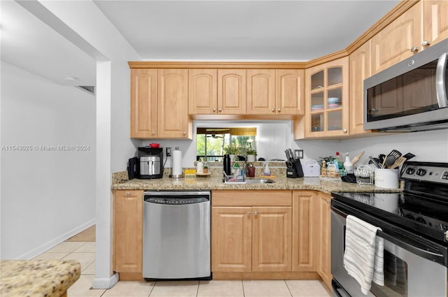 kitchen with light stone countertops, appliances with stainless steel finishes, light brown cabinets, sink, and light tile floors