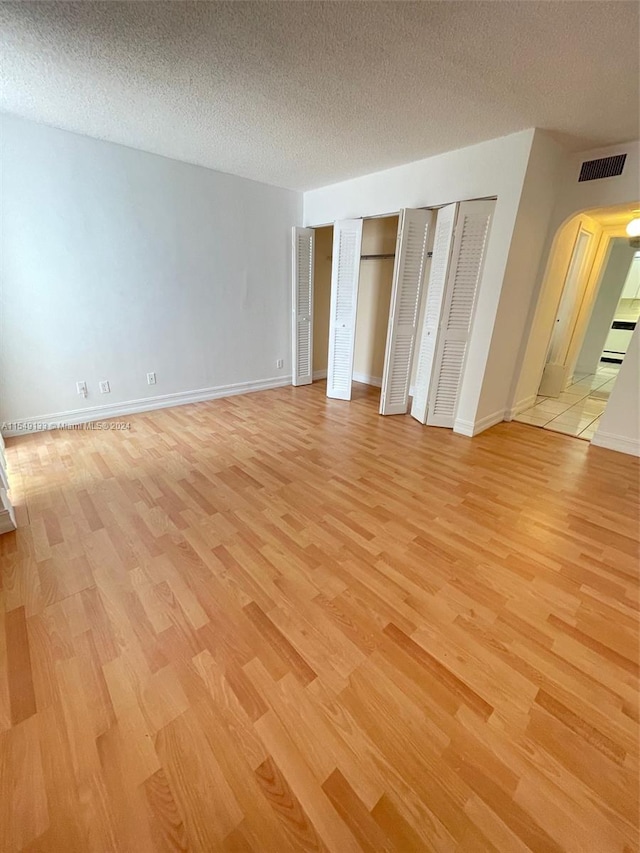 unfurnished bedroom featuring light hardwood / wood-style floors, two closets, and a textured ceiling