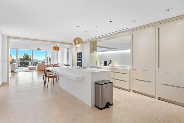 kitchen featuring hanging light fixtures, sink, light hardwood / wood-style flooring, a kitchen island, and black electric stovetop