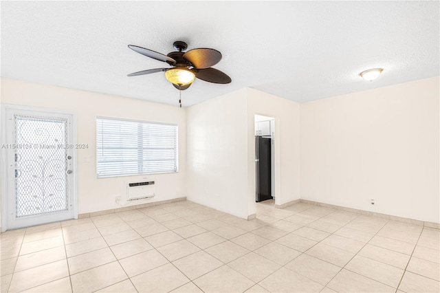 tiled empty room with a wall mounted air conditioner, ceiling fan, and a textured ceiling