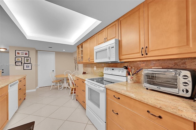 kitchen featuring light tile flooring, light stone countertops, white appliances, backsplash, and a tray ceiling