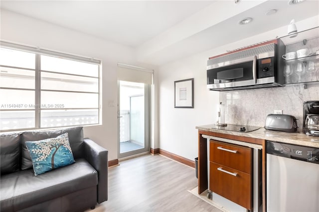 kitchen featuring appliances with stainless steel finishes, light hardwood / wood-style flooring, light stone counters, and decorative backsplash