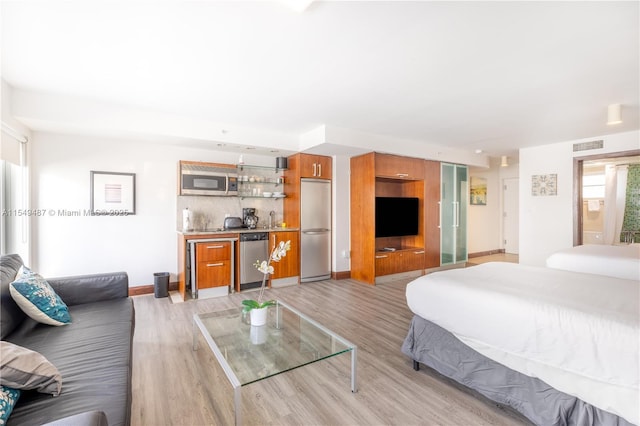 bedroom with built in refrigerator, wet bar, and light hardwood / wood-style floors