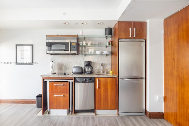 kitchen with tasteful backsplash, stainless steel appliances, sink, and light wood-type flooring