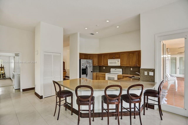 kitchen featuring white appliances, sink, a high ceiling, kitchen peninsula, and a breakfast bar area