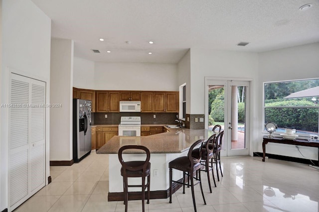 kitchen featuring white appliances, light tile patterned floors, a kitchen breakfast bar, french doors, and kitchen peninsula