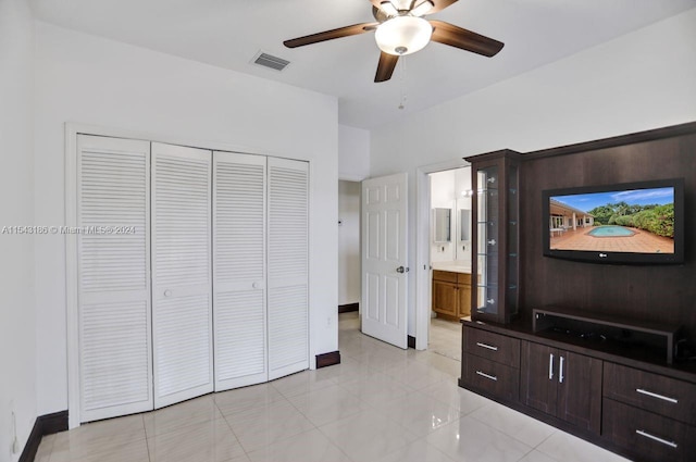 bedroom featuring a closet, ceiling fan, light tile patterned floors, and ensuite bath