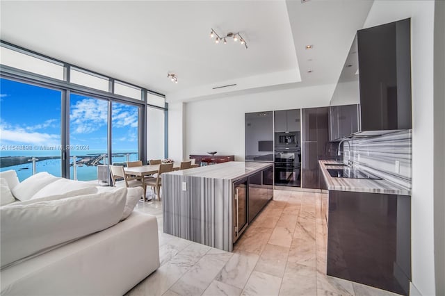 kitchen featuring expansive windows, black appliances, a water view, light tile floors, and dark brown cabinetry