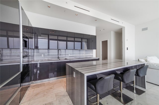 kitchen featuring sink, light tile floors, light stone counters, backsplash, and a kitchen bar