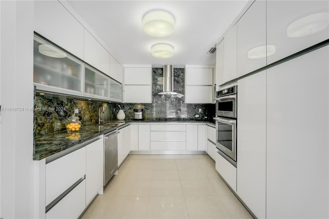 kitchen with backsplash, light tile flooring, dark stone counters, wall chimney range hood, and white cabinetry