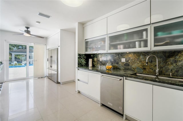 kitchen featuring light tile flooring, white cabinetry, backsplash, dark stone countertops, and ceiling fan