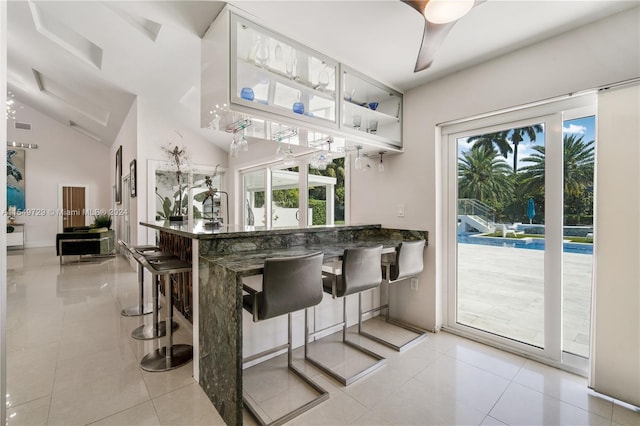 kitchen with light tile flooring, a kitchen bar, dark stone counters, ceiling fan, and lofted ceiling