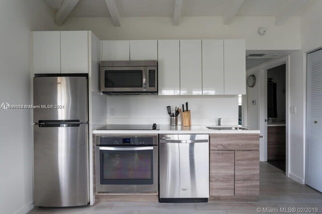 kitchen featuring beam ceiling, light wood-type flooring, appliances with stainless steel finishes, and white cabinetry