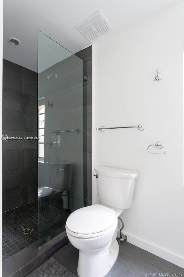 bathroom featuring toilet, a shower with door, and tile flooring