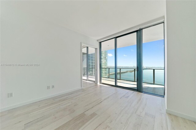 spare room featuring floor to ceiling windows, light hardwood / wood-style floors, and a water view