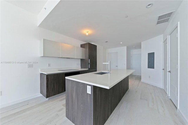 kitchen featuring an island with sink, dark brown cabinetry, sink, and light wood-type flooring