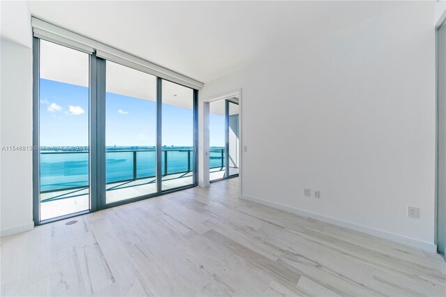 empty room featuring floor to ceiling windows, a water view, and light wood-type flooring