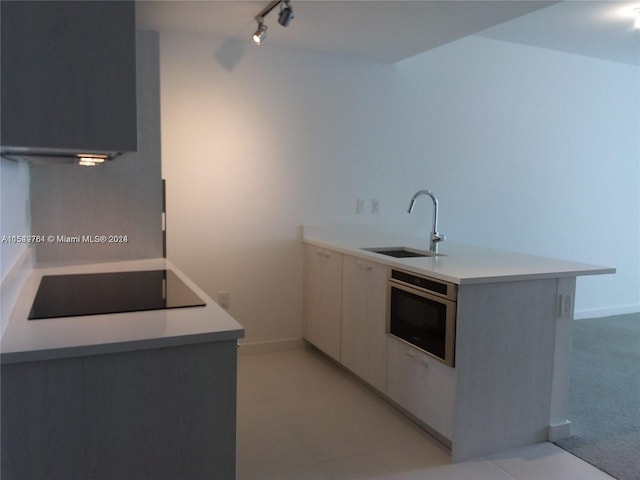 kitchen with light tile flooring, black electric cooktop, track lighting, oven, and sink