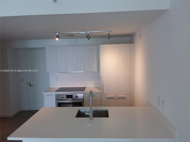 kitchen featuring rail lighting, cooktop, sink, and oven