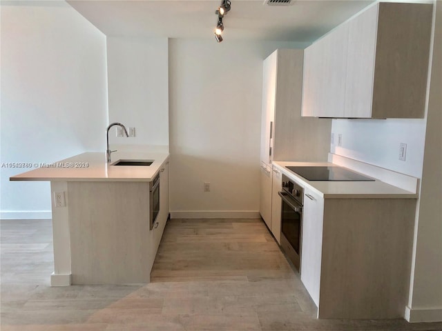 kitchen featuring rail lighting, stainless steel oven, black electric stovetop, light wood-type flooring, and sink