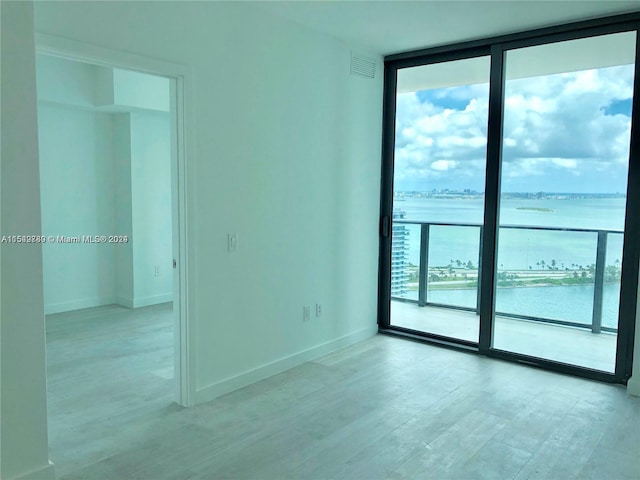 spare room with a water view, expansive windows, and light wood-type flooring