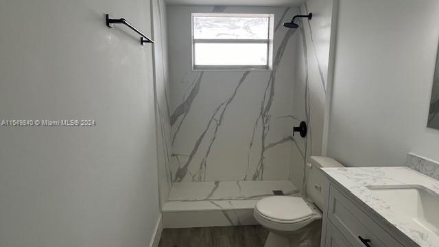 bathroom with hardwood / wood-style flooring, toilet, vanity, and tiled shower