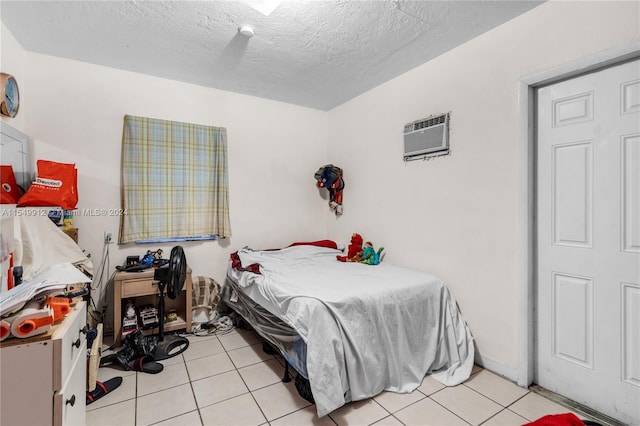 bedroom featuring a wall unit AC, light tile patterned floors, and a textured ceiling