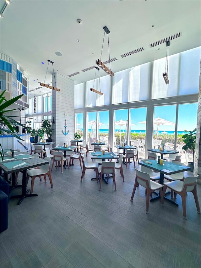 carpeted dining space featuring a water view, a wall of windows, and a high ceiling