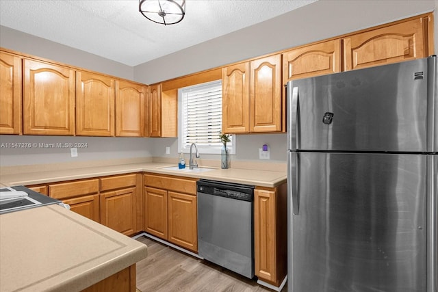 kitchen with a textured ceiling, sink, appliances with stainless steel finishes, and light wood-type flooring