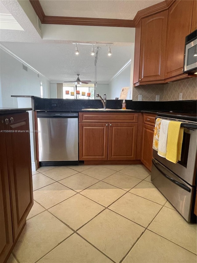 kitchen featuring ceiling fan, appliances with stainless steel finishes, rail lighting, tasteful backsplash, and ornamental molding