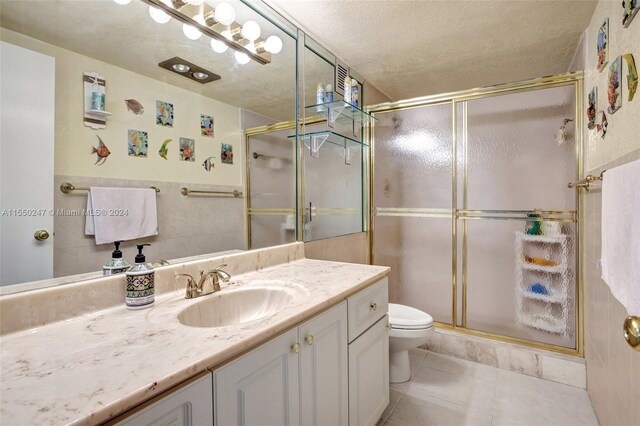 bathroom with toilet, an enclosed shower, a textured ceiling, large vanity, and tile floors