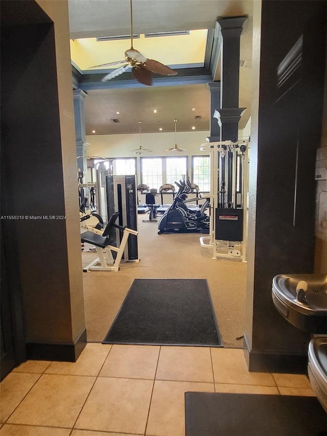 gym with decorative columns, ceiling fan, and light tile floors