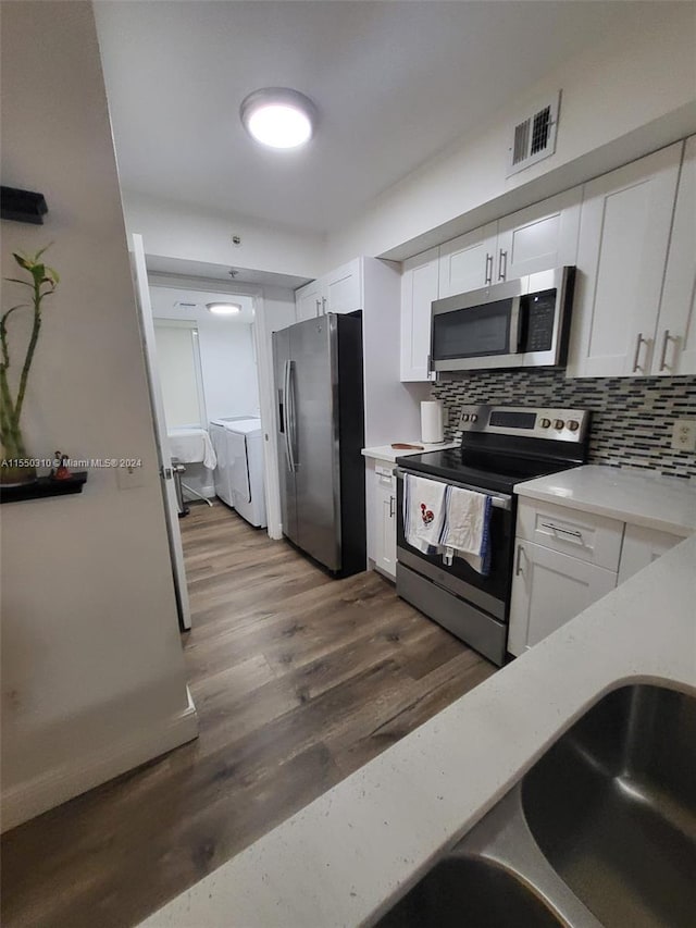 kitchen featuring backsplash, stainless steel appliances, white cabinets, washer and dryer, and dark hardwood / wood-style flooring