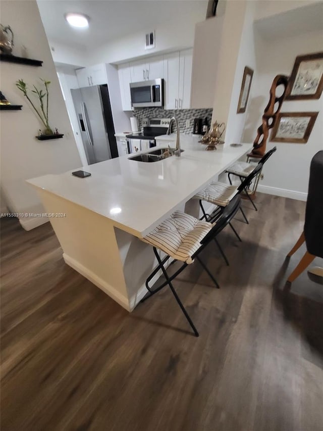 kitchen with dark hardwood / wood-style floors, kitchen peninsula, appliances with stainless steel finishes, a breakfast bar area, and tasteful backsplash