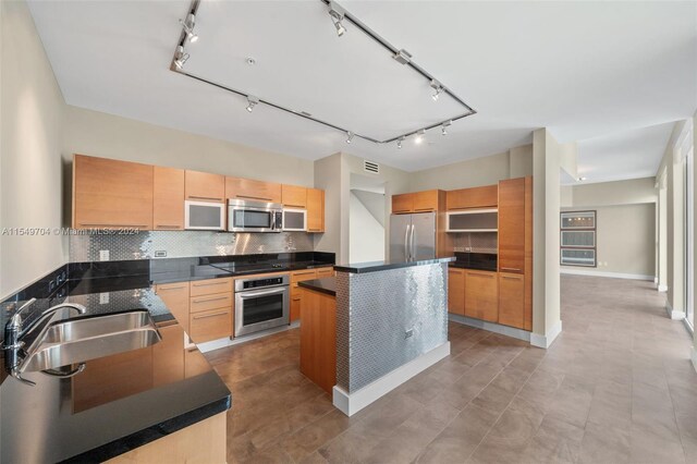 kitchen featuring stainless steel appliances, track lighting, tasteful backsplash, sink, and a center island