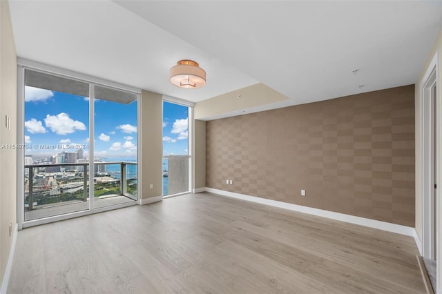 unfurnished room featuring a water view, light hardwood / wood-style flooring, and a wall of windows