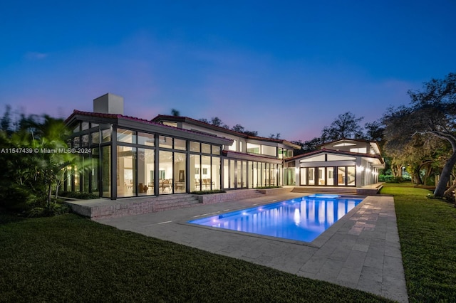 pool at dusk with a patio and a lawn