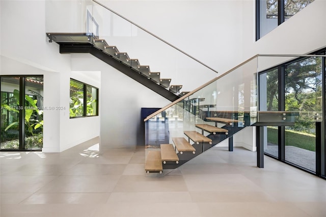 stairs with a wealth of natural light, a towering ceiling, and light tile flooring