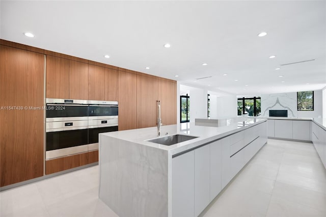 kitchen featuring sink, white cabinets, light tile flooring, and a kitchen island with sink