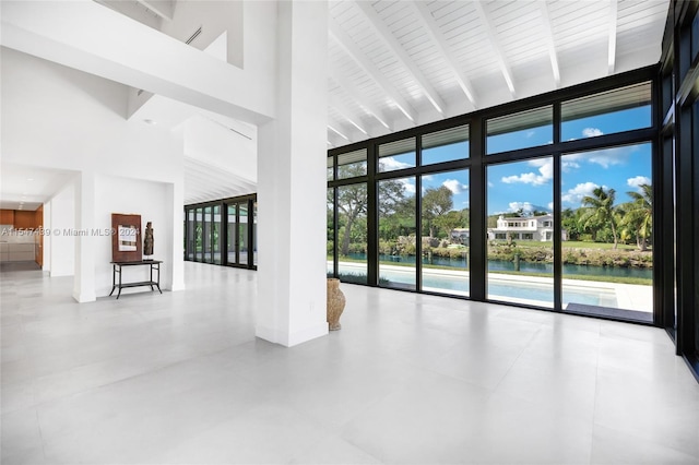 unfurnished room featuring tile flooring, beamed ceiling, a water view, expansive windows, and high vaulted ceiling