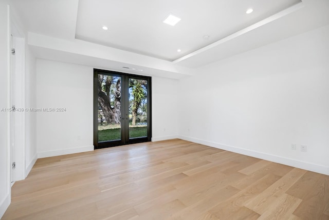 spare room with a tray ceiling, light hardwood / wood-style flooring, and french doors