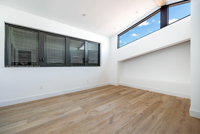 empty room featuring beamed ceiling, high vaulted ceiling, and light wood-type flooring