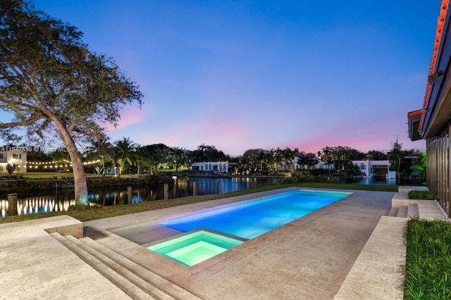 pool at dusk featuring an in ground hot tub, a patio area, and a water view