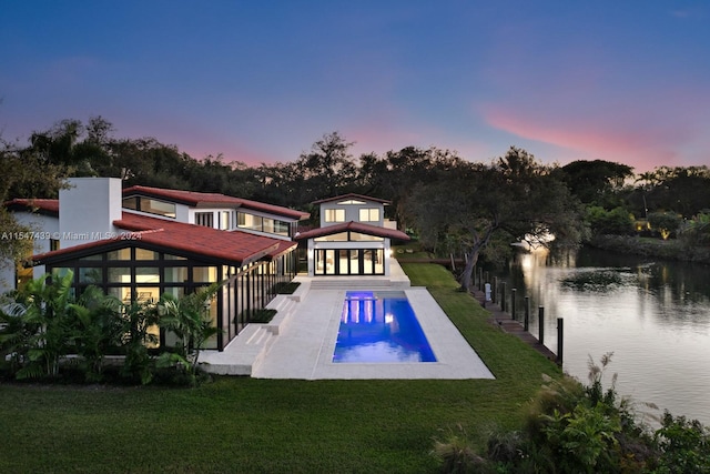 pool at dusk with a water view and a lawn