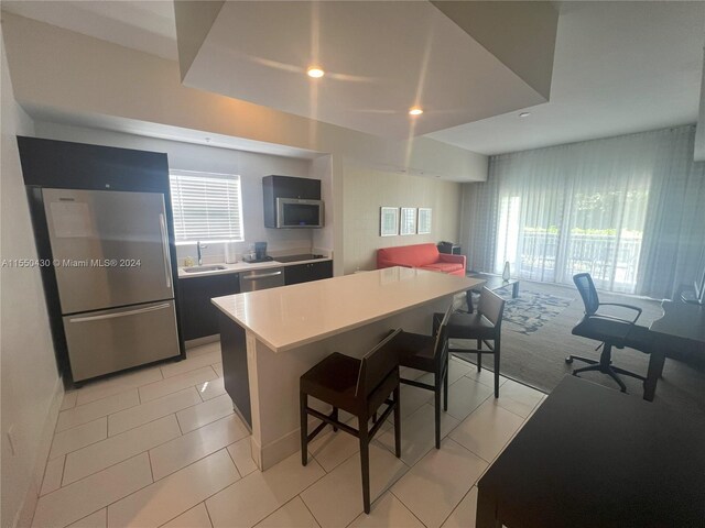 kitchen featuring a kitchen bar, light tile patterned flooring, stainless steel appliances, sink, and a center island