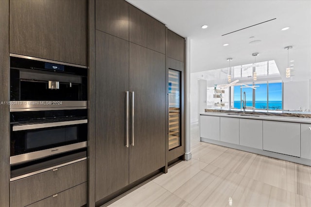 kitchen with stainless steel double oven, hanging light fixtures, white cabinets, light tile flooring, and dark brown cabinetry