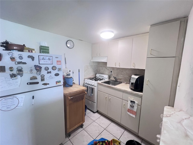 kitchen with backsplash, gas range, light tile floors, white cabinets, and white refrigerator