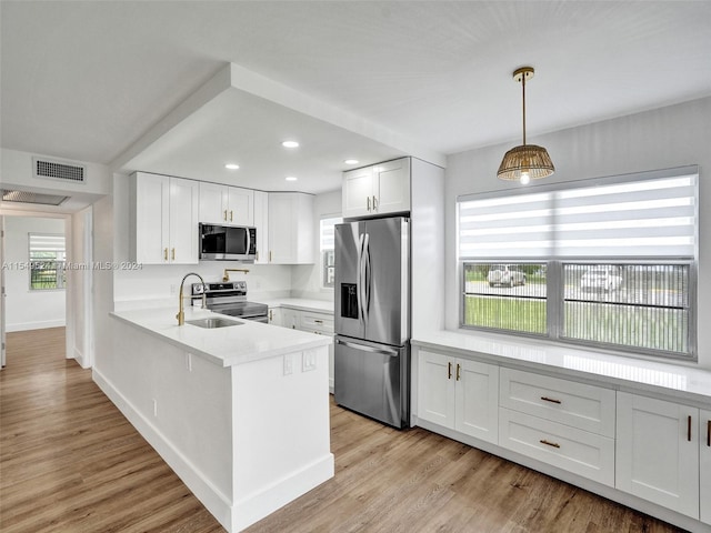 kitchen featuring light wood-type flooring, hanging light fixtures, appliances with stainless steel finishes, and white cabinetry